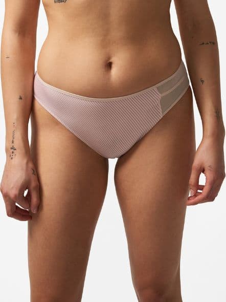 Person wearing pink striped underwear with sheer side panels, standing against a white background. Visible tattoos on arms.